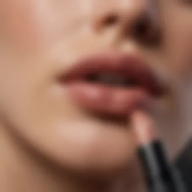 Close-up of a hand applying MAC nude lipstick on lips.